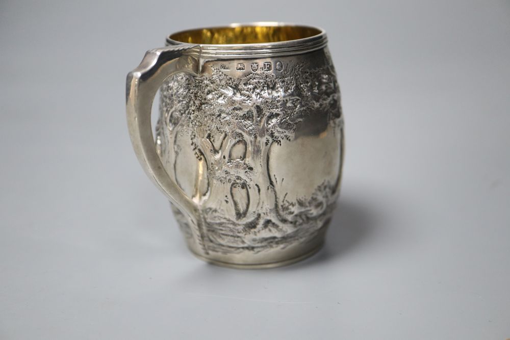 A George III silver barrel shaped christening mug, embossed with figures at play in woodland scene,